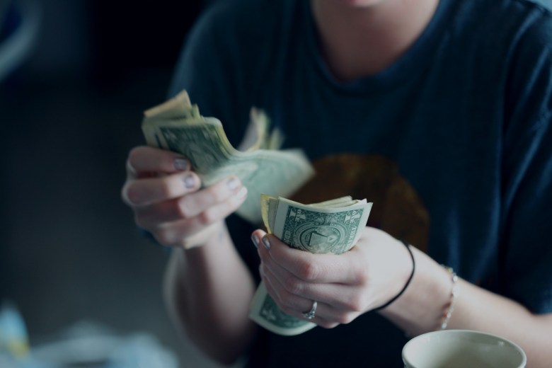 Woman counting one dollar bills to pay for cheap TEFL TESOL online certification course.